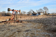 #10: Oil production activity in this area, a oil well pump in front and an oil gathering facility at background