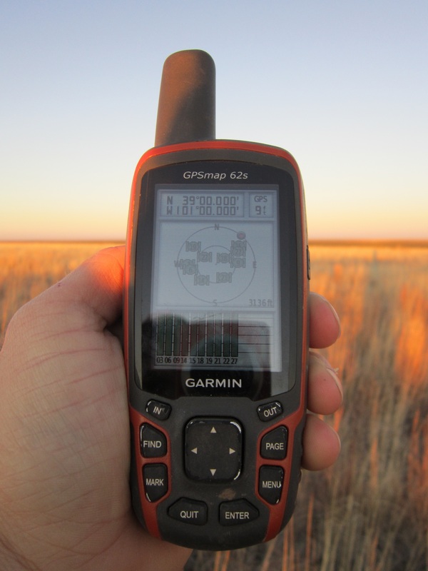 GPS at confluence point, showing elevation and accuracy, as well ground cover in the background.