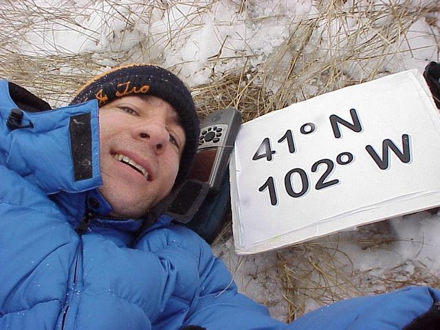 Geographer Joseph Kerski lying on the grass and snow at the confluence site.