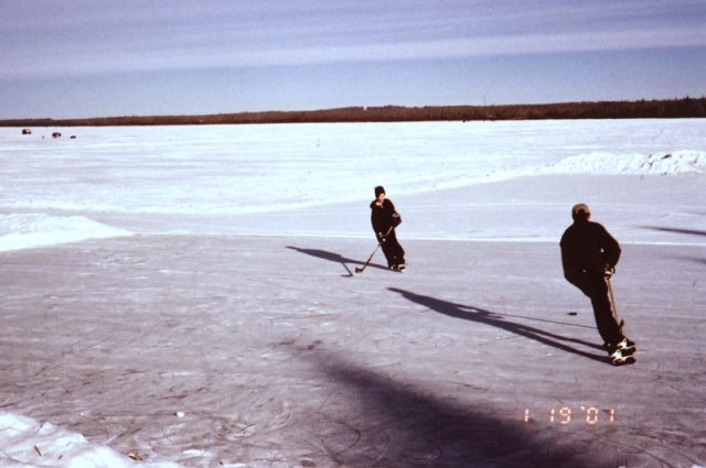 A father and son practice hockey on the lake.