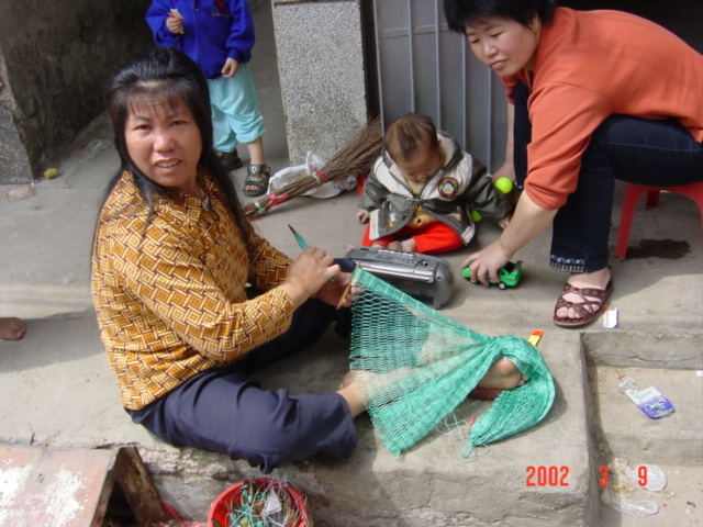 Womenfolk sitting outside their homes weaving nets