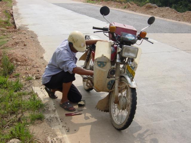 Motorcyclist repairing bike in hot sun