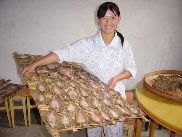 Pyjama-clad guesthouse proprietress proudly displaying dried fish