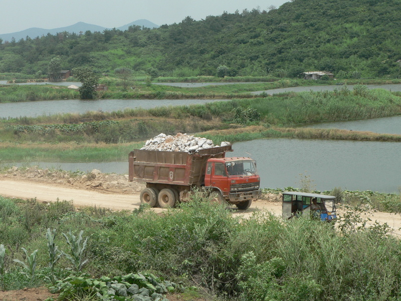 A truck loaded with rocks rumbles past our waiting three-wheeler 