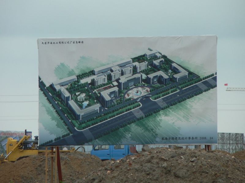 Sign depicting future factory development, with work going on behind