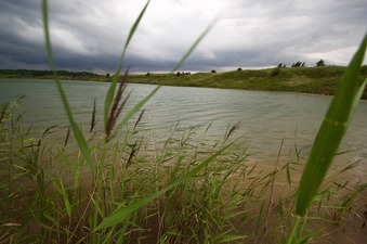 #1: The confluence point lies in this large pond, 23m away.  (This is also a view to the West; note the approaching thunderstorm.)