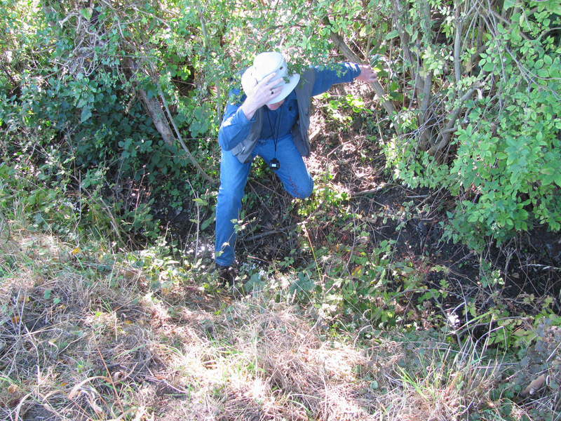 Alan makes his way through a ditch and brambles with sharp thorns.