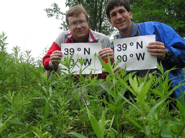 Bob Coulter and Joseph Kerski proudly display signs in the tall plants at the confluence site.
