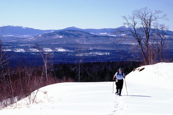 Snowshoeing over the crest of a hill with the Western Mountains in the background